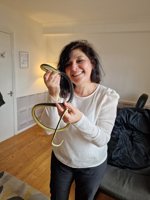 A smiling woman holding a snake indoors, with a sofa and a closed door in the background.